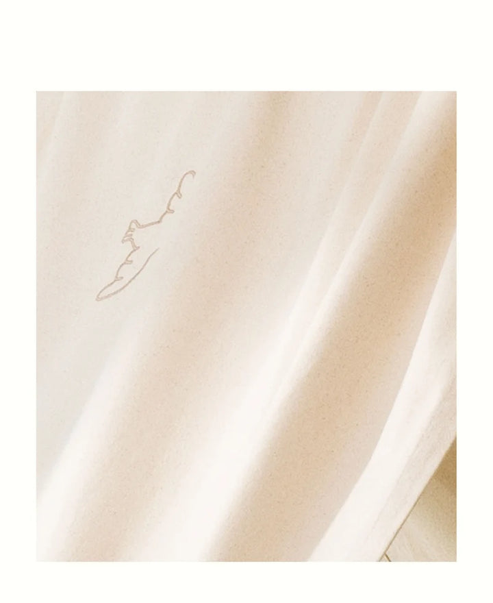 A close-up of draped cream-colored fabric with a subtle, tonal embroidered flying bird on the upper left.