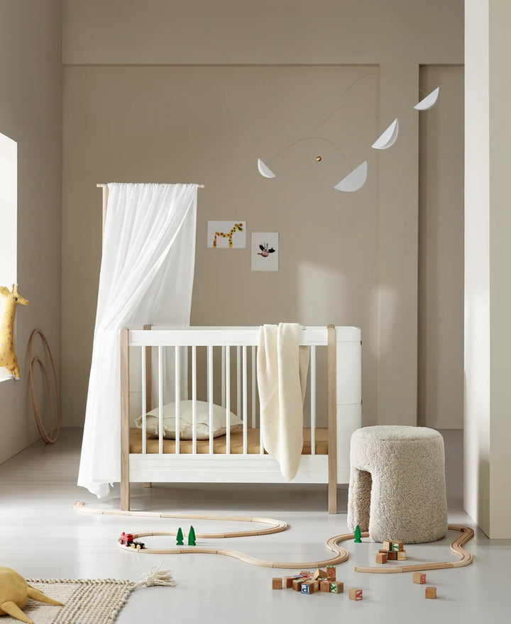 Oliver furniture Mini + cot in a nursery setting with a white linen canopy over the cot 