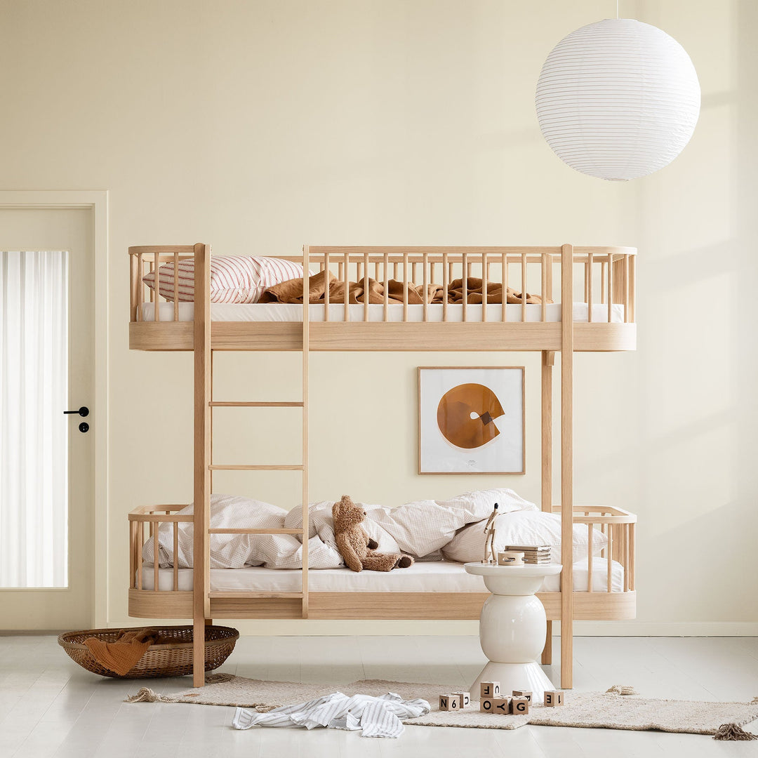 Oliver Furniture Wooden bunk bed in oak in a minimalistic room with a lamp and artwork on the wall.