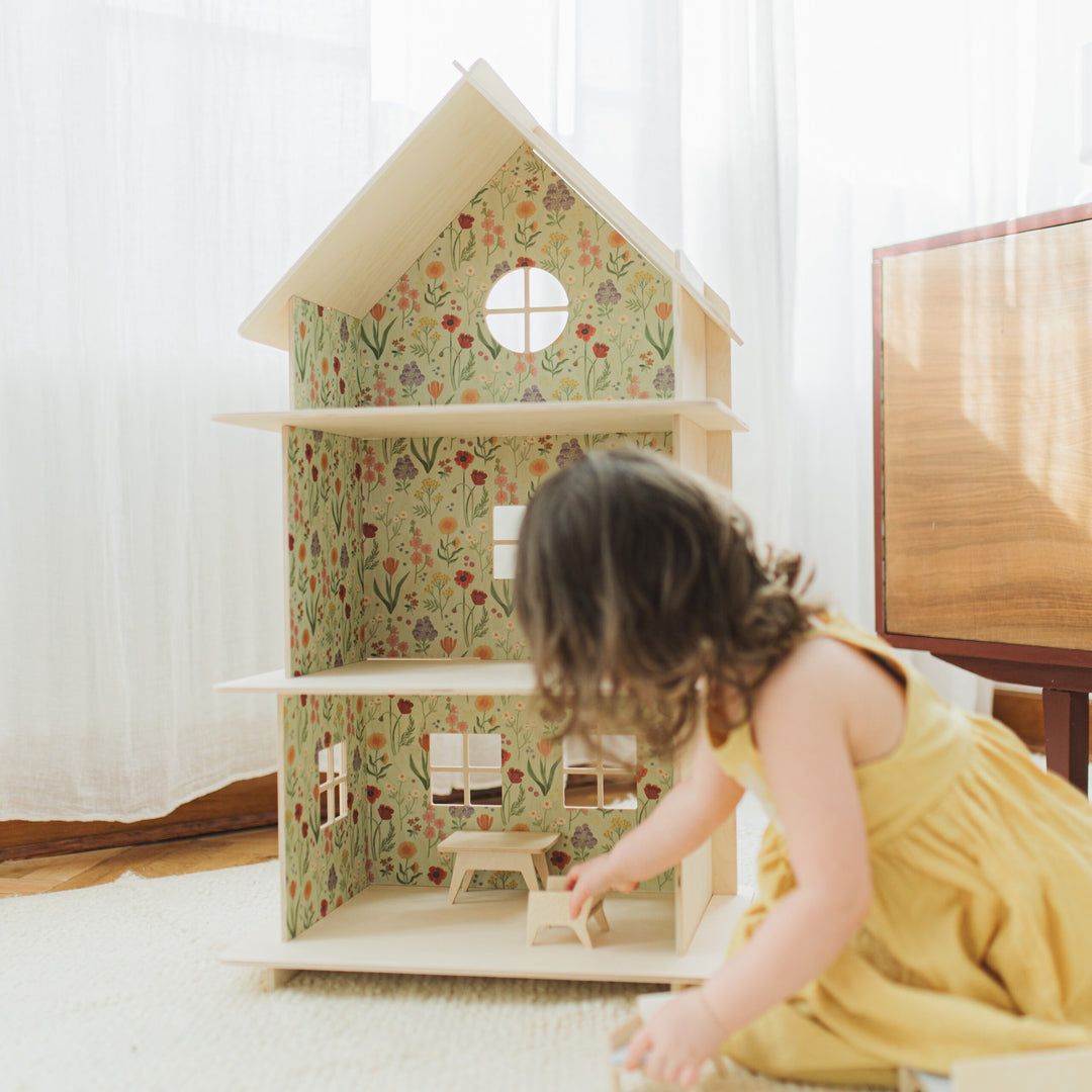 Hand placing furniture into the dollhouse with floral wallpaper.
