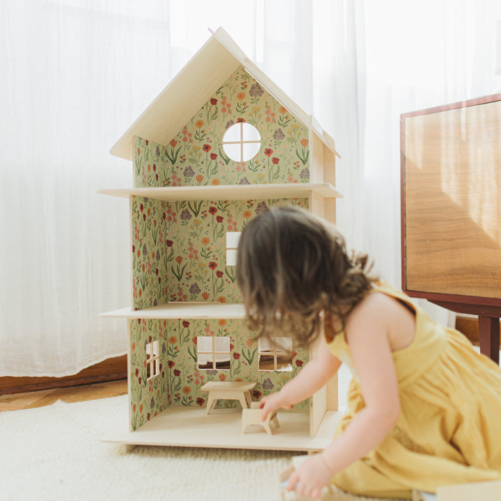 Hand placing furniture into the dollhouse with floral wallpaper.