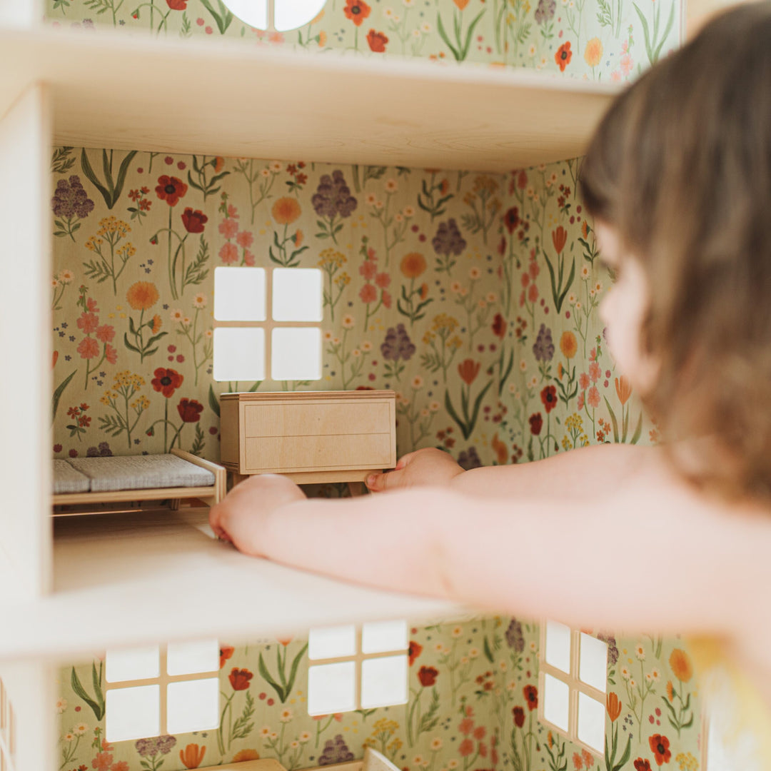 Hand placing furniture in a dollhouse with floral wallpaper.