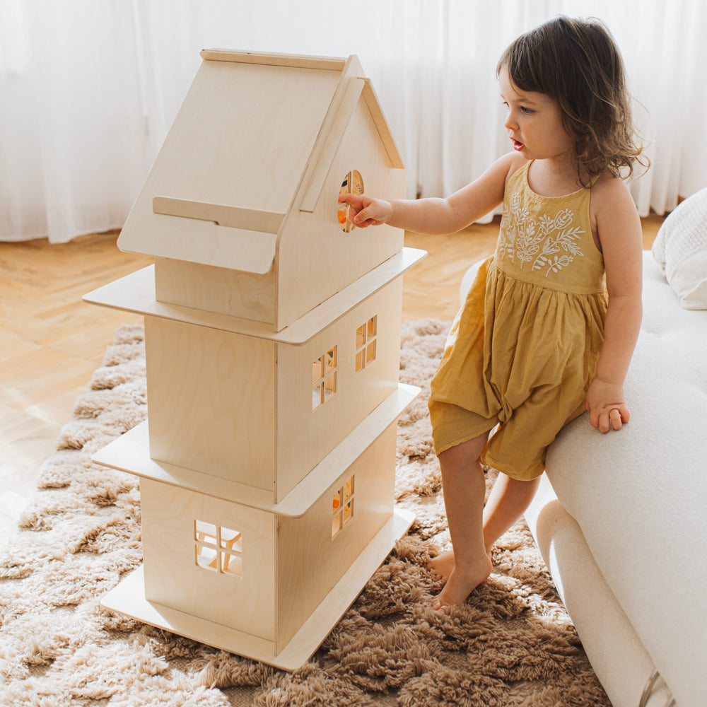 Child playing with a wooden dollhouse on a carpeted floor.