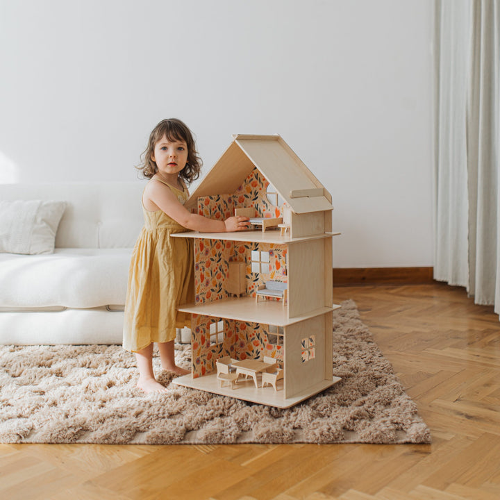 Child playing with a dollhouse in a room with a white couch and wooden floor.